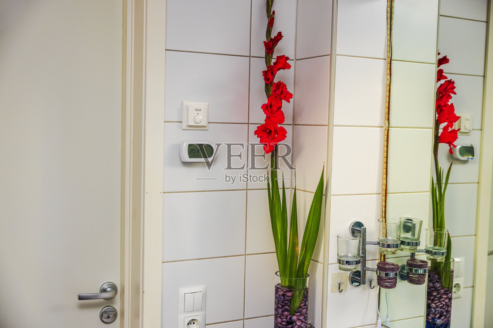 优雅的浴室内部设有红色剑兰在高水晶花瓶在台面，旁边的镜子和水槽与配件。照片摄影图片