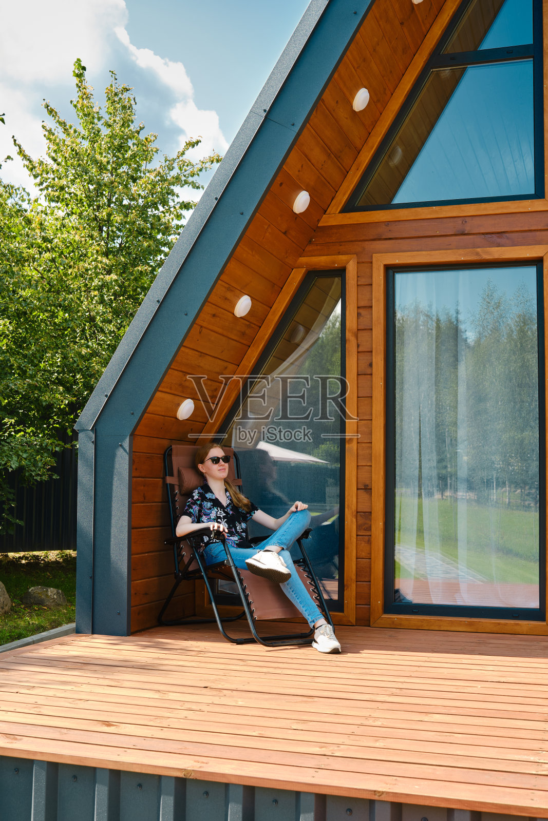 女人在阳光明媚的日子里在现代的框架小屋露台上放松照片摄影图片