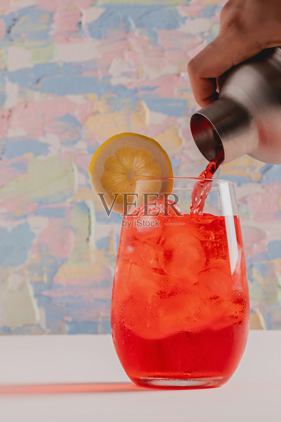 鸡尾酒调酒器提供红色饮料的玻璃杯，柠檬片。照片摄影图片