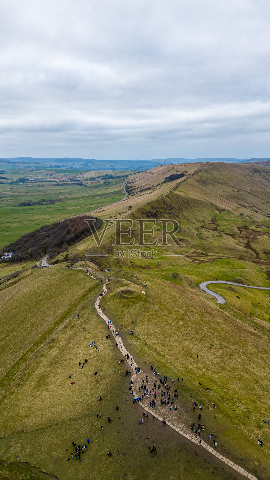 在英国的皮克区，在多云的天空下，在郁郁葱葱的绿色景观下，徒步旅行者在蜿蜒的小径上鸟瞰。照片摄影图片