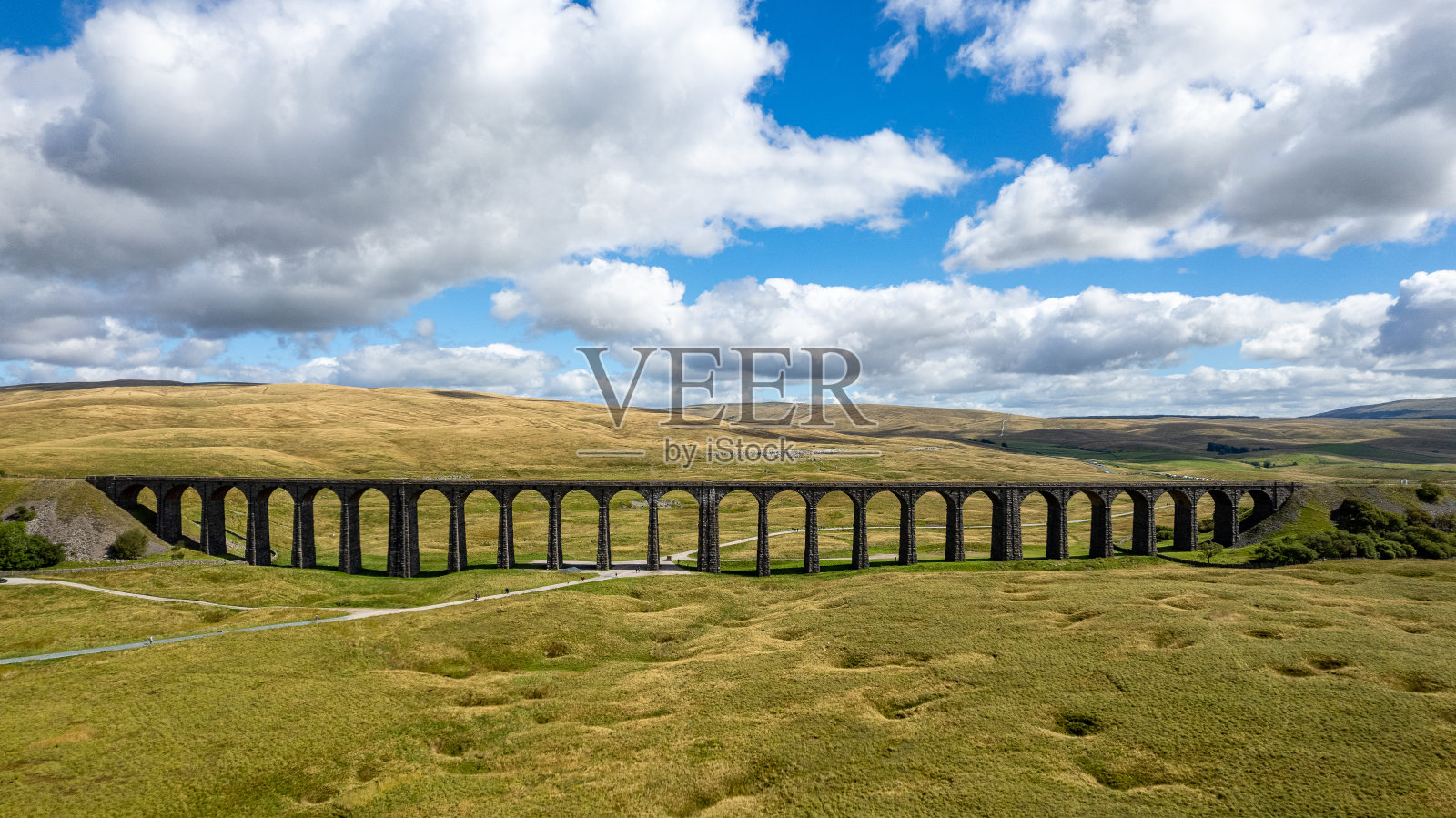 多云的天空下，郁郁葱葱的绿色景观中，一座古老的高架桥的美景。照片摄影图片