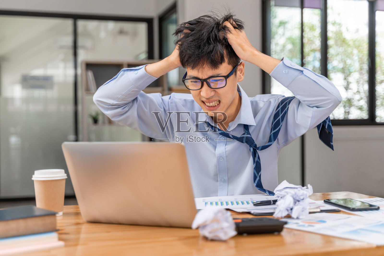 沮丧和愤怒的年轻商人在办公室工作到很晚，试图完成他的项目照片摄影图片