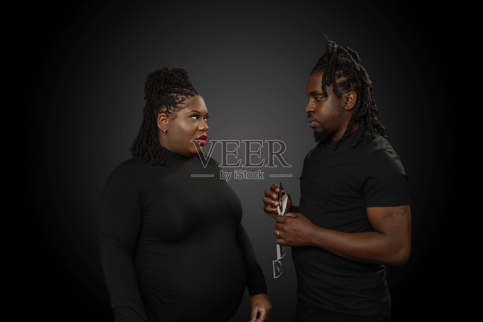 一对即将成为非裔美国人父母的夫妇在一间工作室里看着他们孩子的超声波照片，背景是深灰色的照片摄影图片