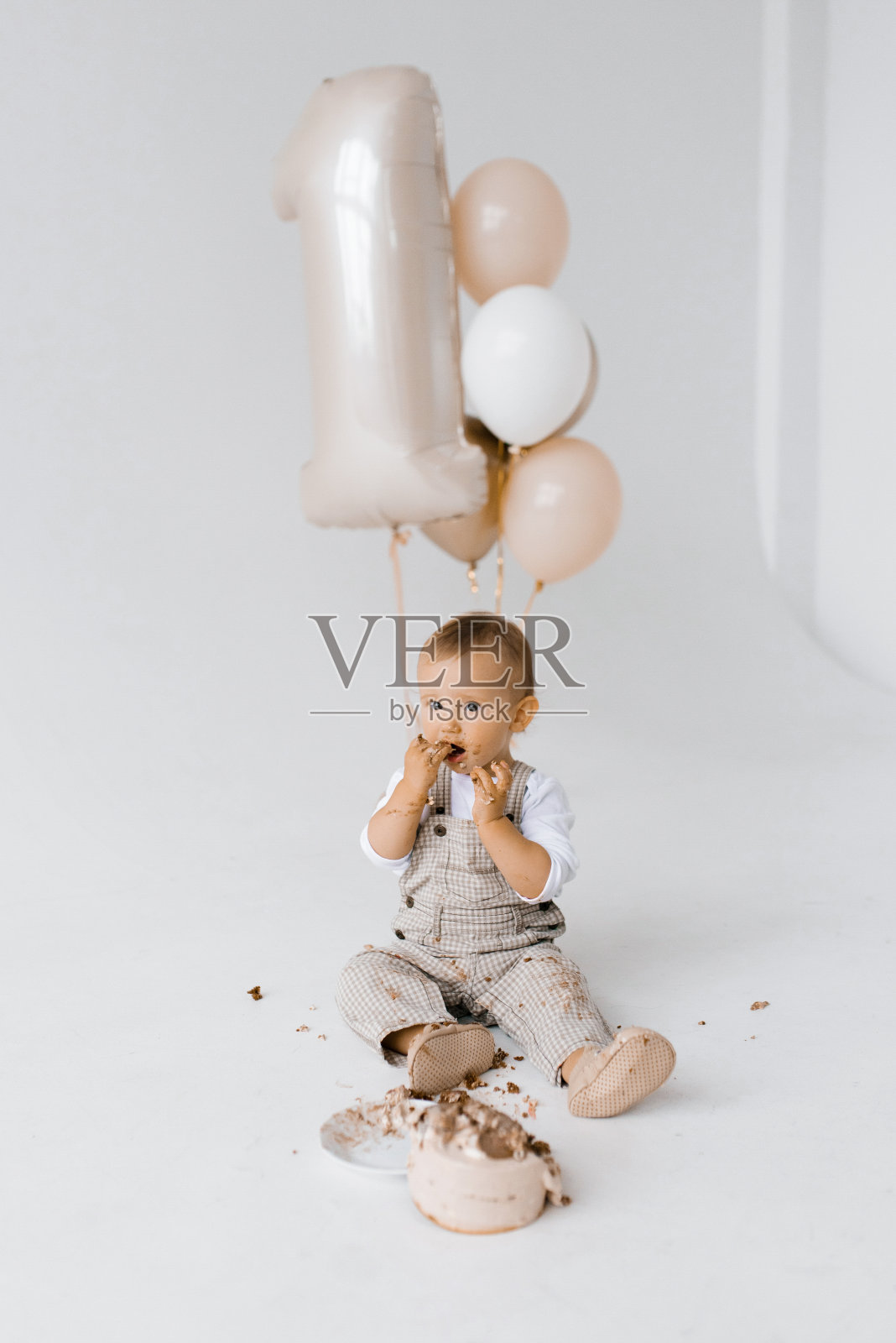 可爱的一岁小男孩吃他的第一个生日蛋糕，背景是一堆气球，上面有数字1照片摄影图片