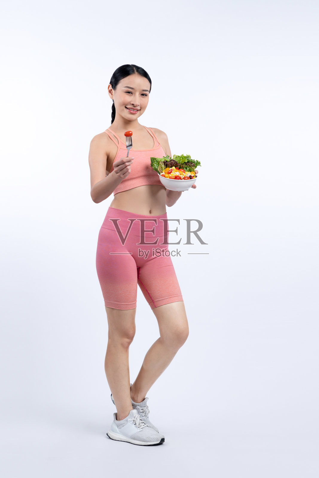 穿着运动服的亚洲女人拿着沙拉碗，背景很偏僻。充满活力的照片摄影图片