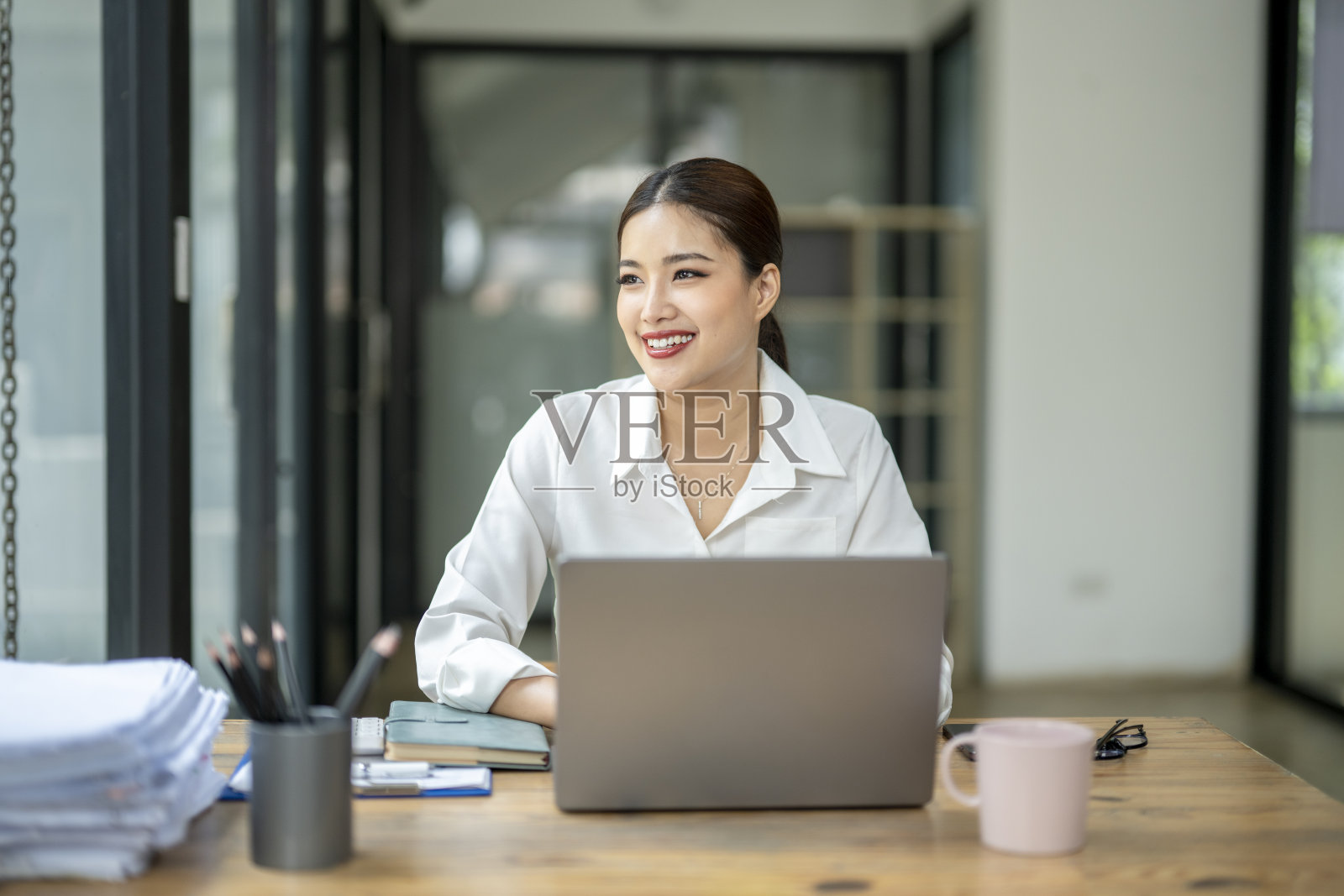 一位女士坐在桌前，手里拿着一台笔记本电脑和一杯咖啡照片摄影图片