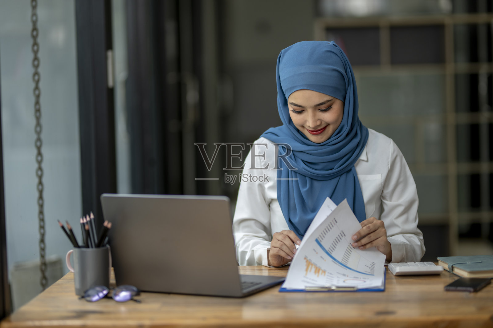 一个戴着蓝色围巾的女人坐在桌子前，手里拿着一台笔记本电脑照片摄影图片