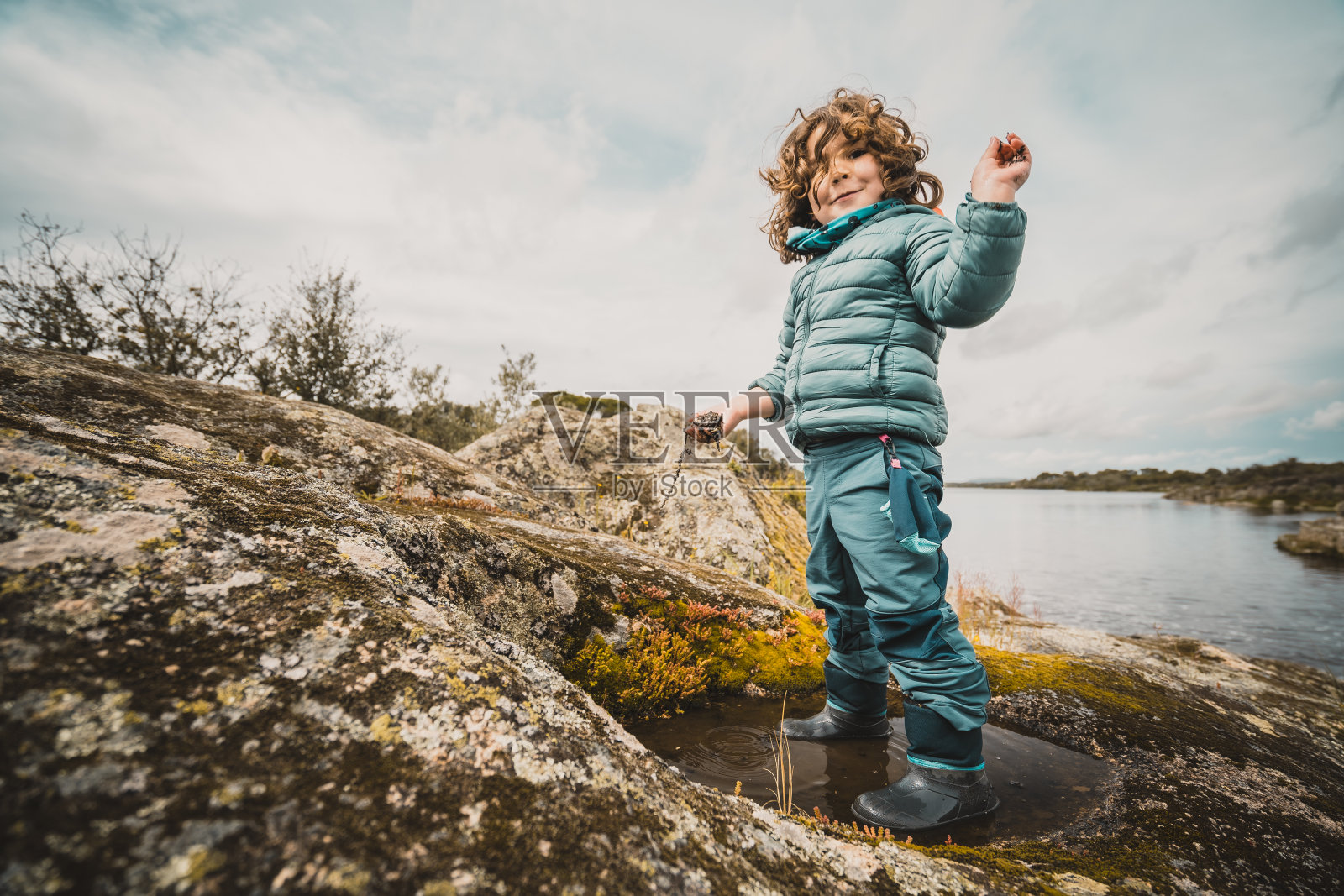 一个小男孩站在水坑里，穿着一件蓝色的夹克照片摄影图片