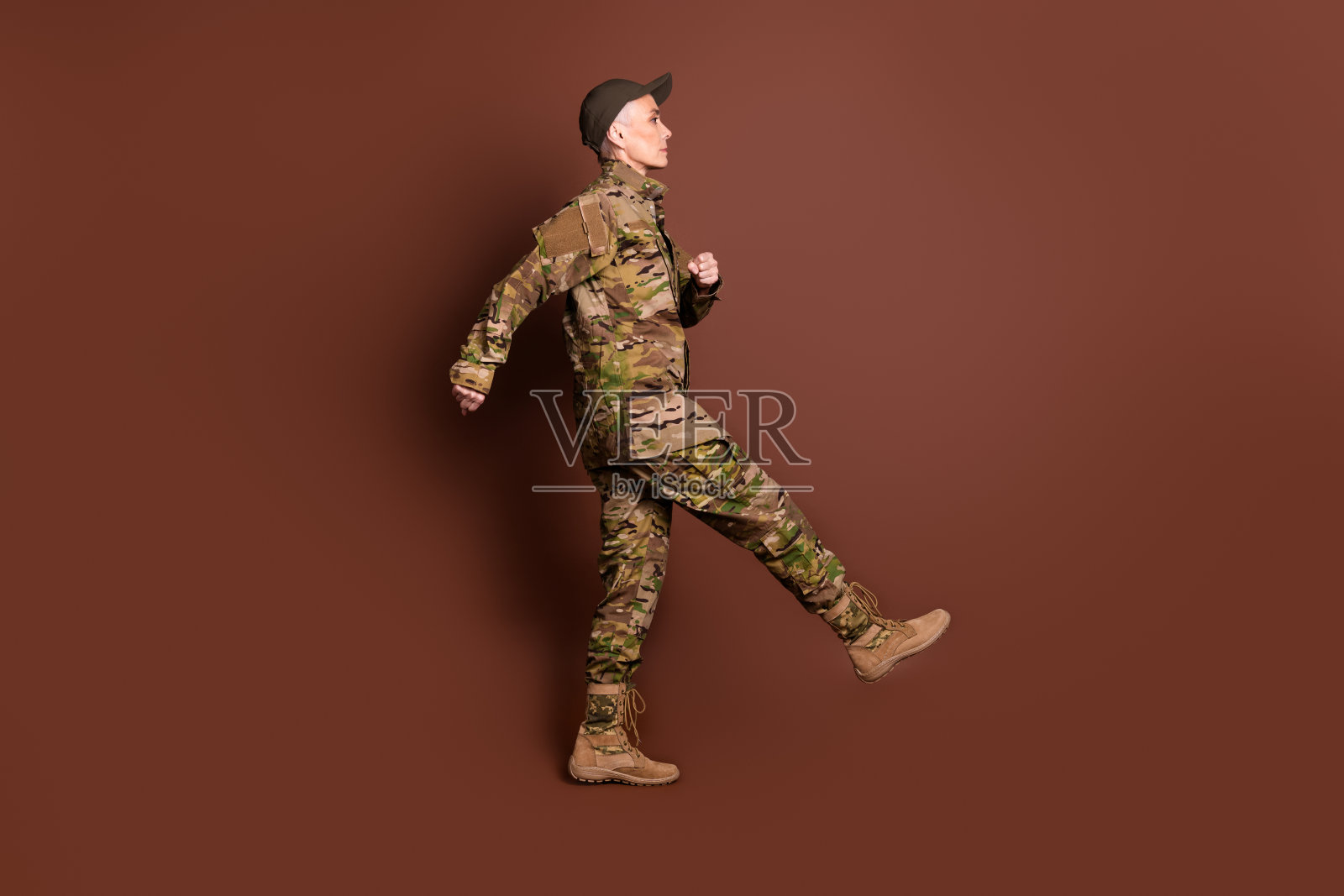 退休女士职业军官步行行军穿着迷彩军装孤立在棕色背景的全长照片照片摄影图片