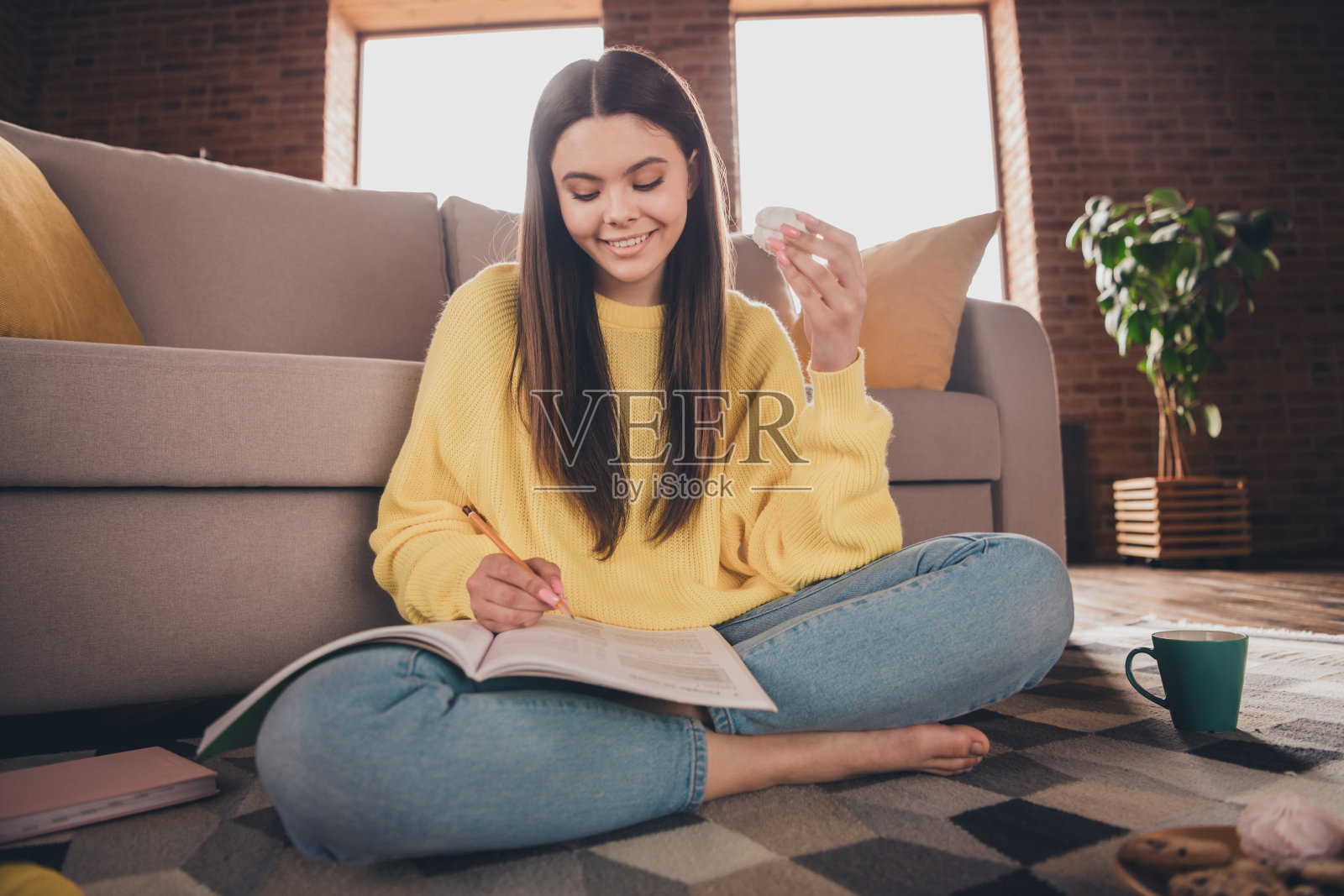 漂亮少女的全尺寸照片坐在地板上做作业吃零食穿着黄色的衣服舒适的日光家室内客厅照片摄影图片