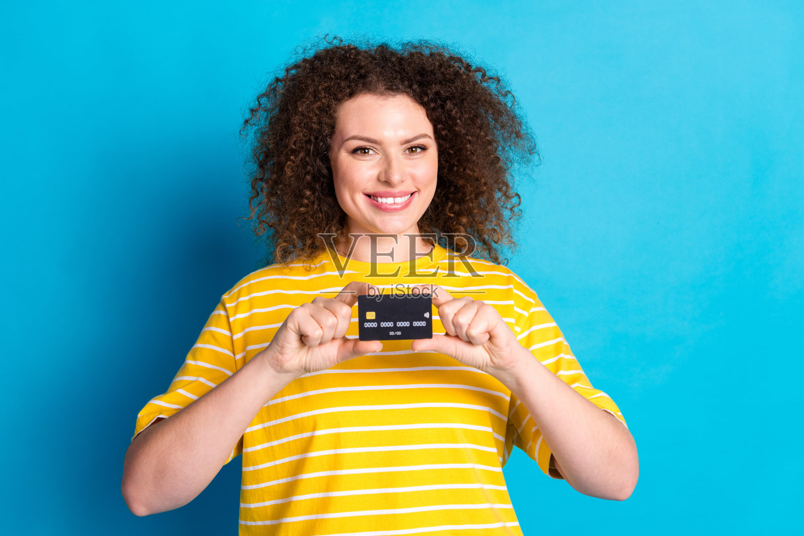 照片肖像可爱的年轻女士手持信用卡穿着时尚的条纹黄色服装孤立的蓝色背景照片摄影图片