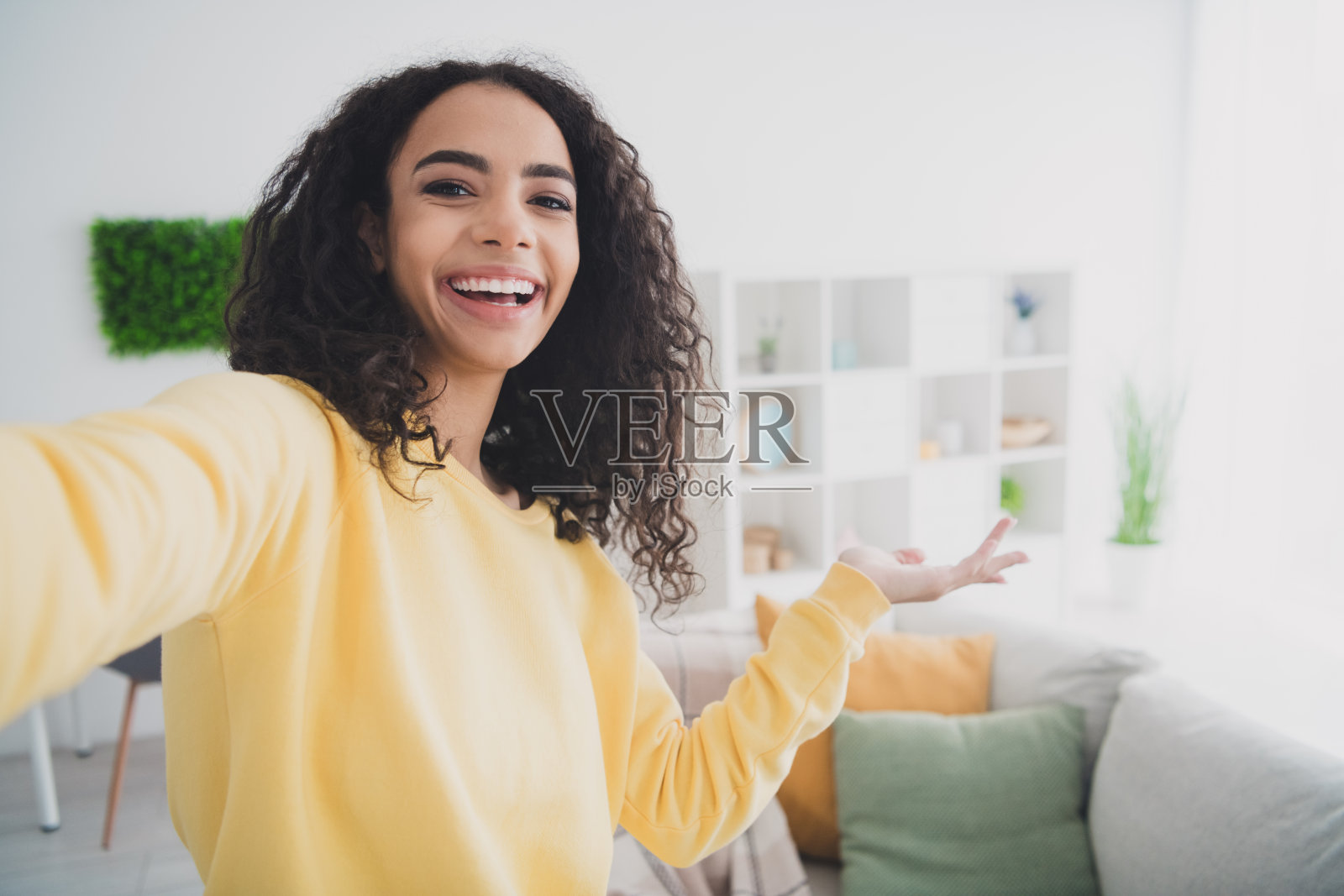 快乐积极的年轻美国女孩的自画像穿着黄色衬衫展示现代设计的家具装修在家里照片摄影图片