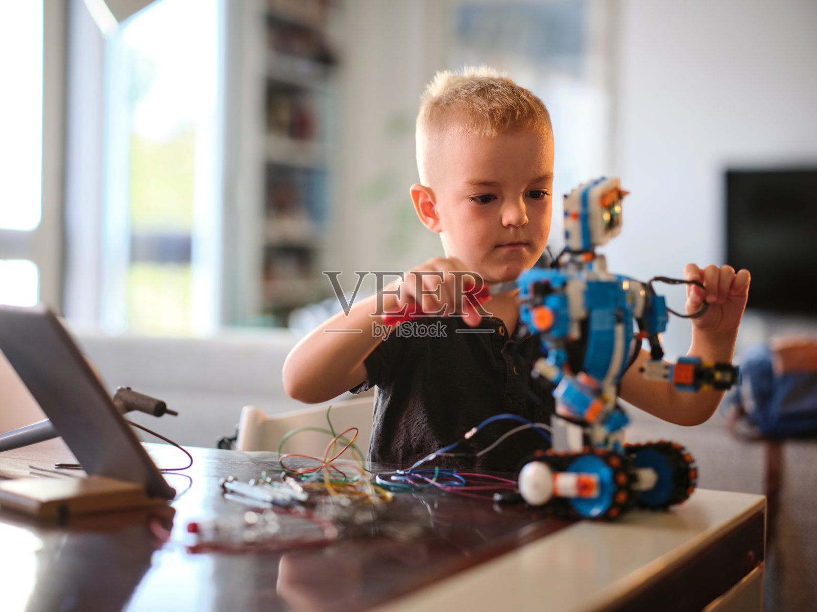 一个小男孩正全神贯注地把电线绑在一个五颜六色的机器人上，一边用桌子上的工具进行动手活动，一边展示创造力和专注力。照片摄影图片