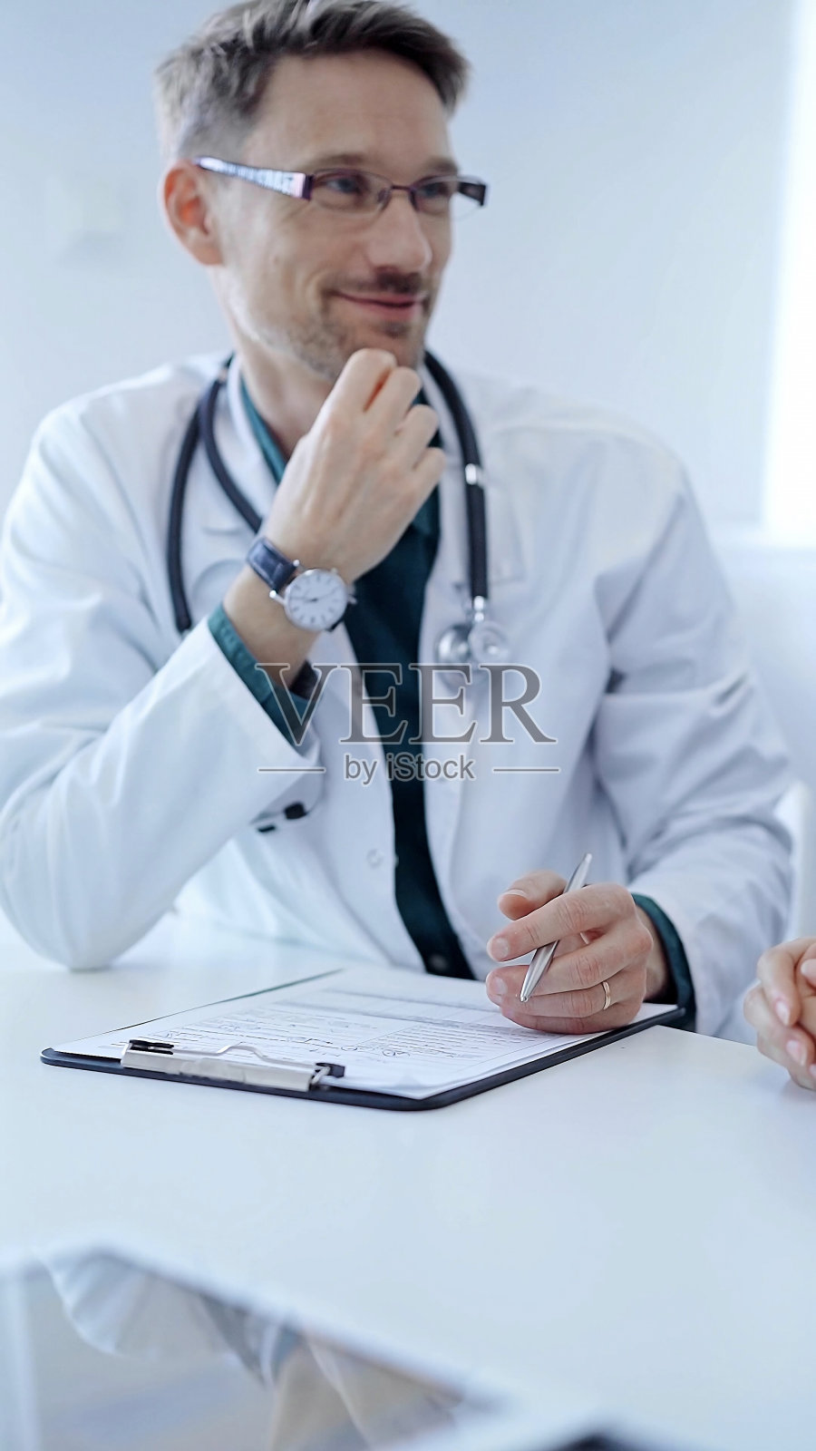 医生和病人。在诊所里，医生在绿色衬衫外面穿了一件白色的大褂，在做手势。医学的概念照片摄影图片