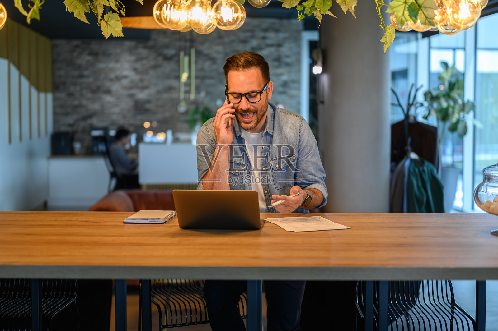 男性自由职业者在办公室的办公桌上通过无线电脑工作，一边打电话一边讨论照片摄影图片