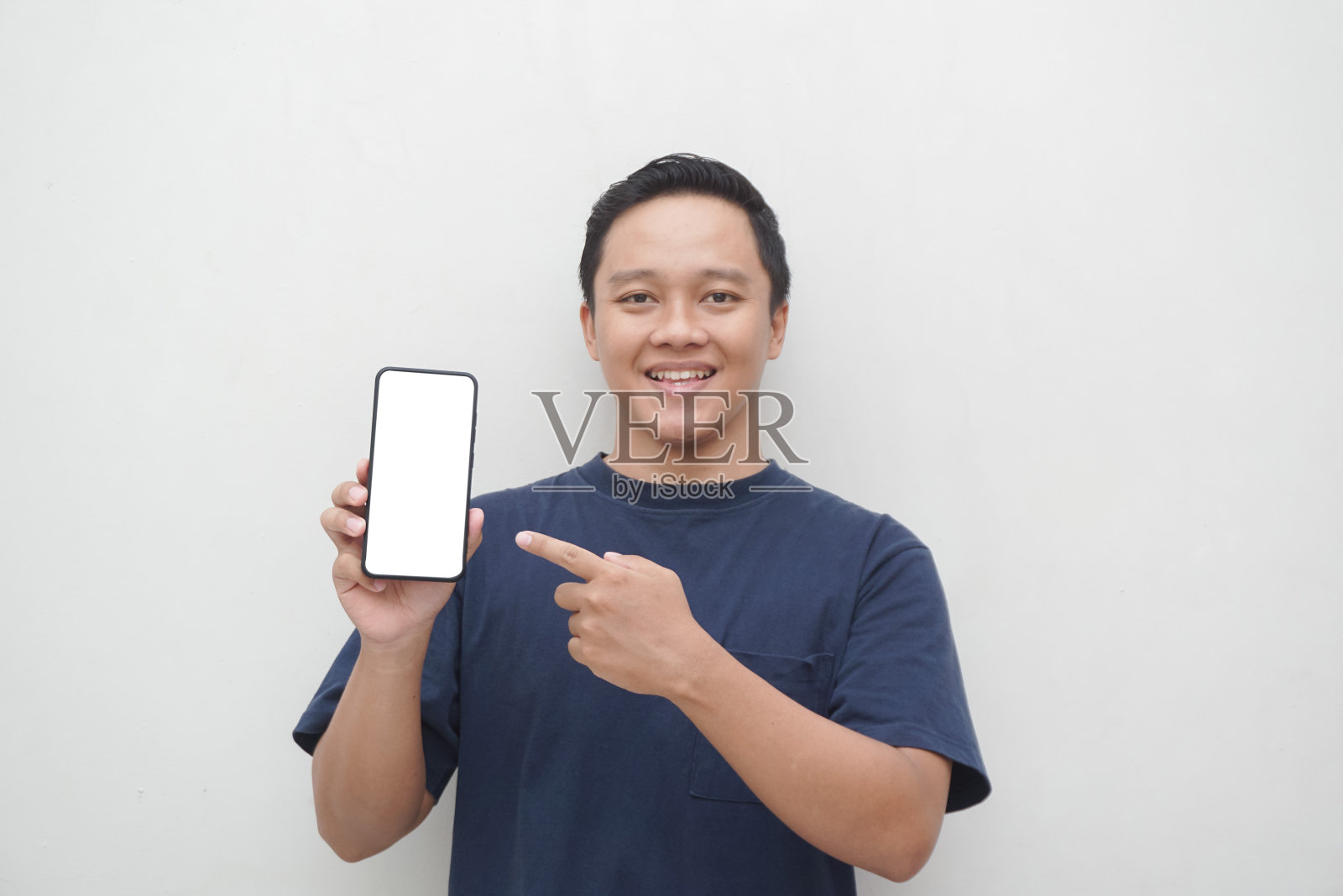 年轻的亚洲男子微笑着指着白色背景下的智能手机屏幕。照片摄影图片