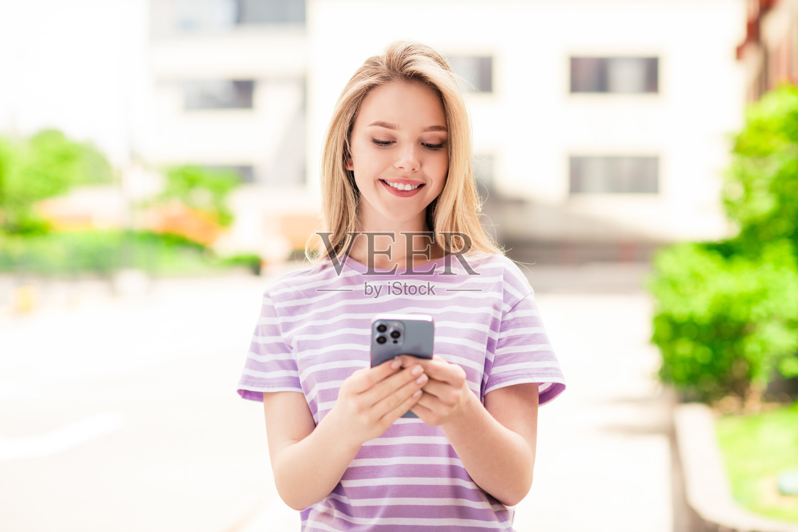 可爱甜美的女士穿着条纹t恤，在城市街道外散步，享受着与现代设备的交流照片摄影图片