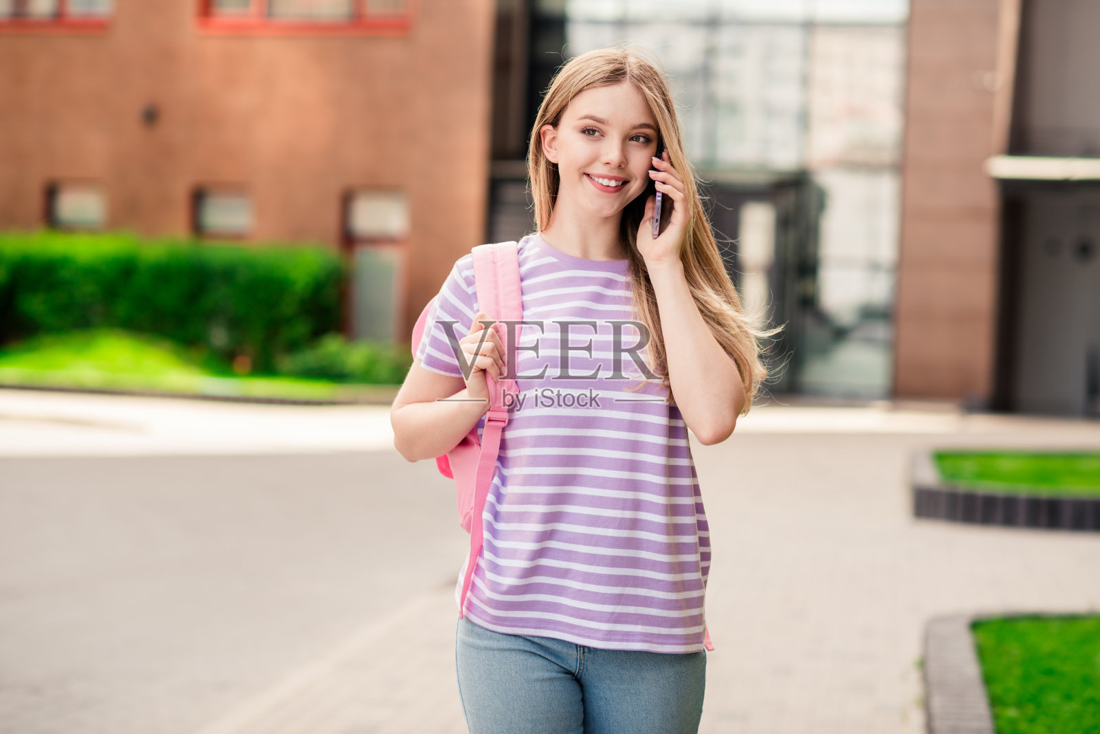 可爱可爱的女士穿着条纹t恤书包，在城市街道外享受着走路说话的现代设备照片摄影图片