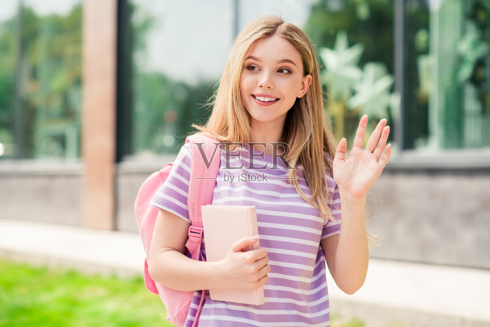 照片中，闪亮可爱的女孩穿着粉色t恤，背着书包，手拿书，在城市户外的步行街上挥舞着手臂照片摄影图片