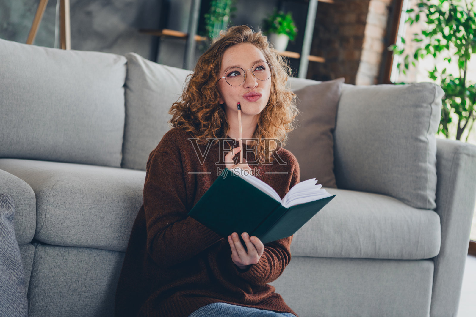 梦幻迷人的女士的照片，穿着时髦的毛衣，坐在地板上，拿着笔记本，写笔记，梦想在室内，房子，家照片摄影图片