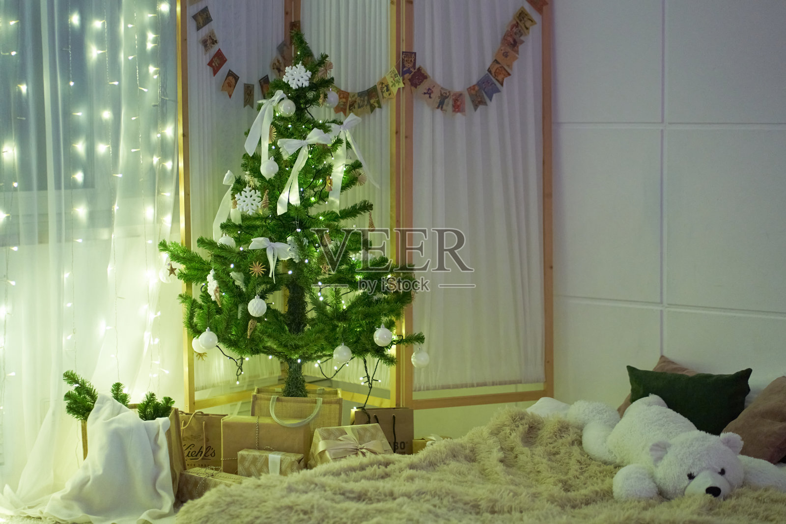 卧室里有舒适的床，枕头，柔软的毛毯，白色的泰迪熊，有球的圣诞树，蝴蝶结，窗帘，花环，礼物。带有复制空间的背景。模板，模型为您的设计照片摄影图片