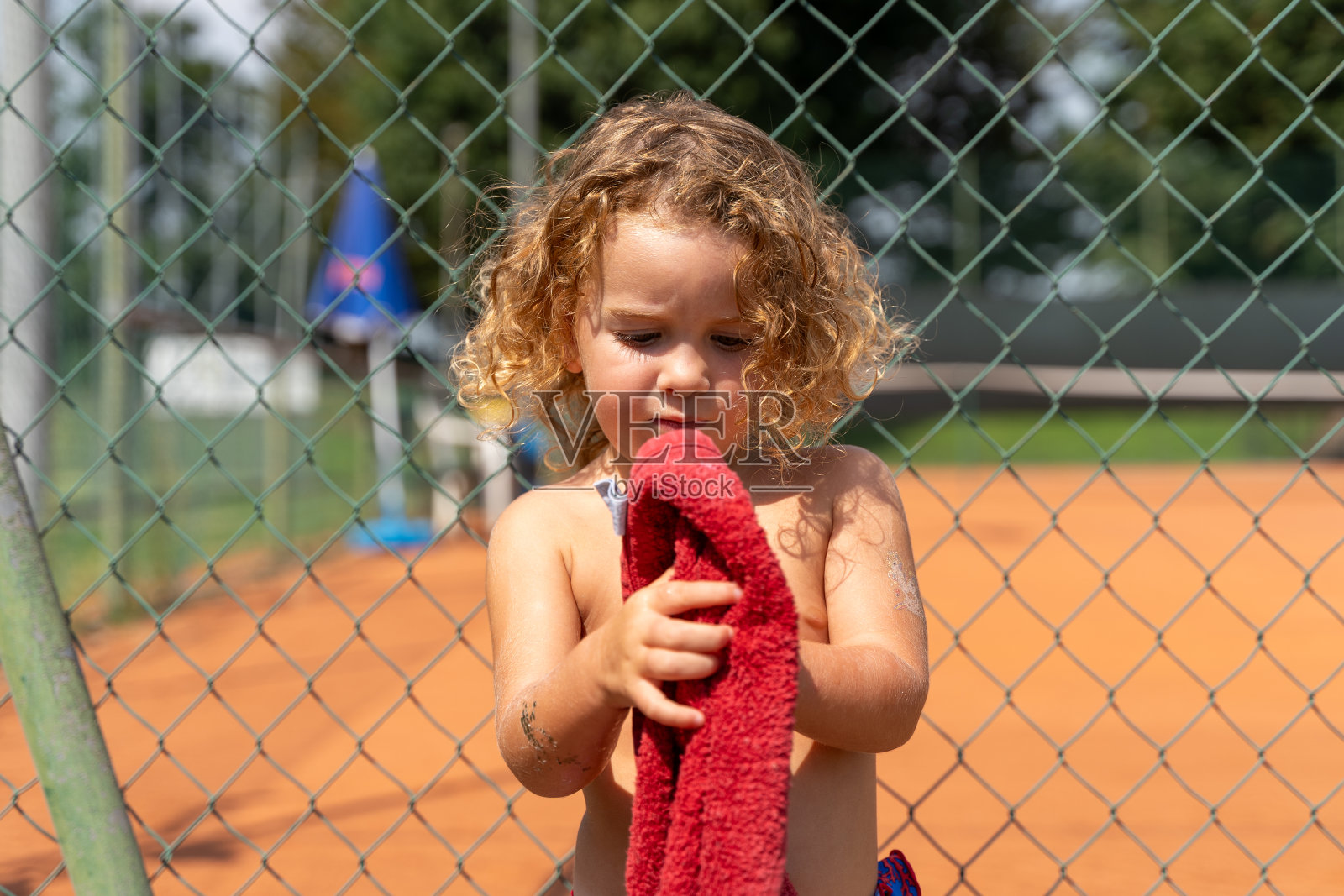 漂亮的肖像，一个2岁的卷发金发女孩玩着一条红毛巾照片摄影图片