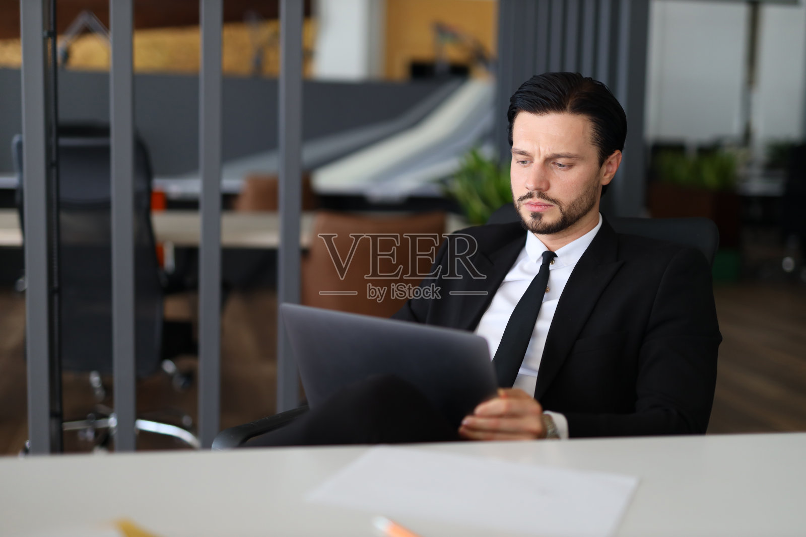 一个西装革履的男人坐在办公桌前，面前放着一台打开的笔记本电脑。他系着领带，全神贯注地工作照片摄影图片