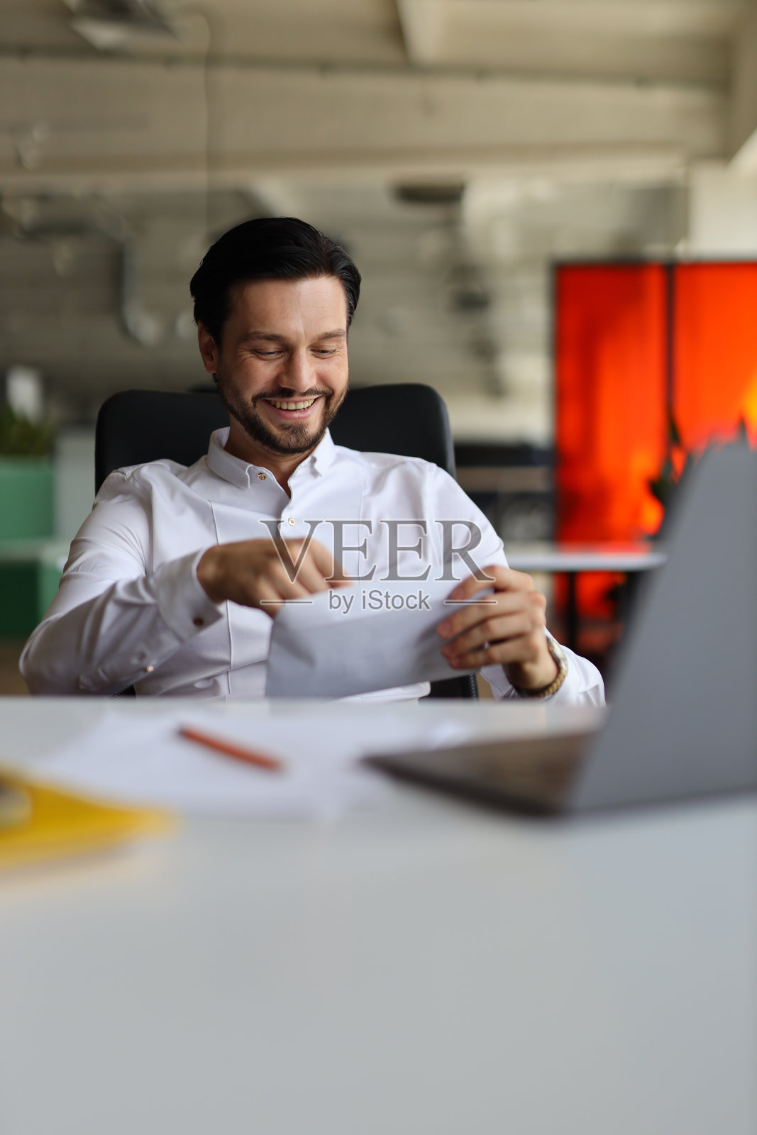 一个男人坐在桌子前，手里拿着一台笔记本电脑和一叠文件。他微笑着打开一张纸照片摄影图片