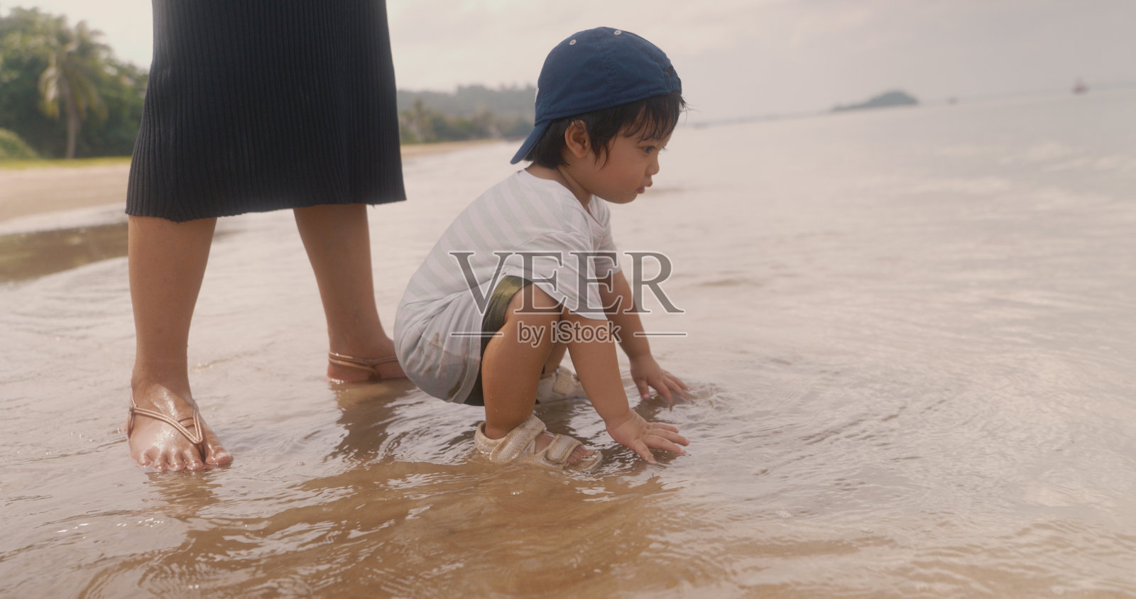 快乐的亚洲男孩在海边度假，和妈妈一起在水里奔跑。男孩在沙滩上玩暑假。美丽的大海、沙滩和蓝天。照片摄影图片