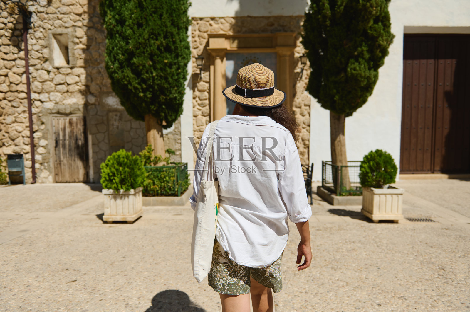 戴着帽子的女人走在石墙和绿树葱葱的历史小镇上照片摄影图片