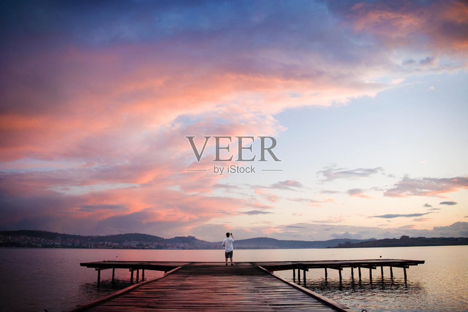 日出时，单身男子在木码头拍摄美丽平静的海景照片摄影图片