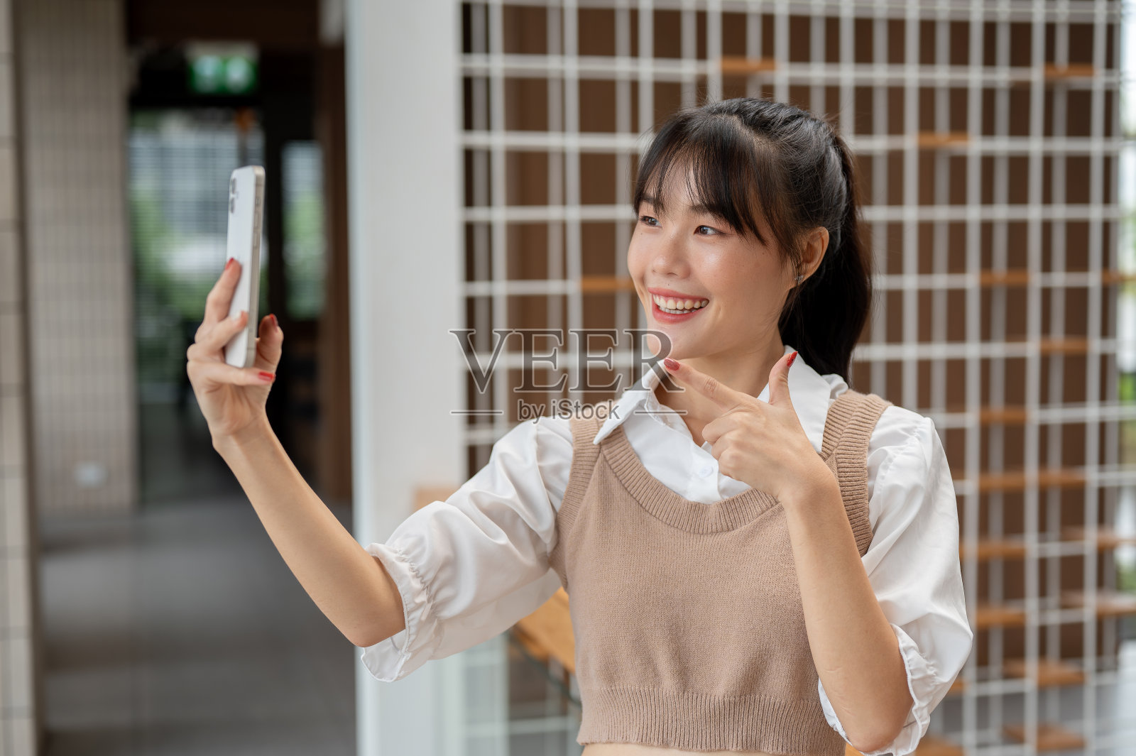 一位迷人的亚洲女性站在大楼里用智能手机自拍。照片摄影图片