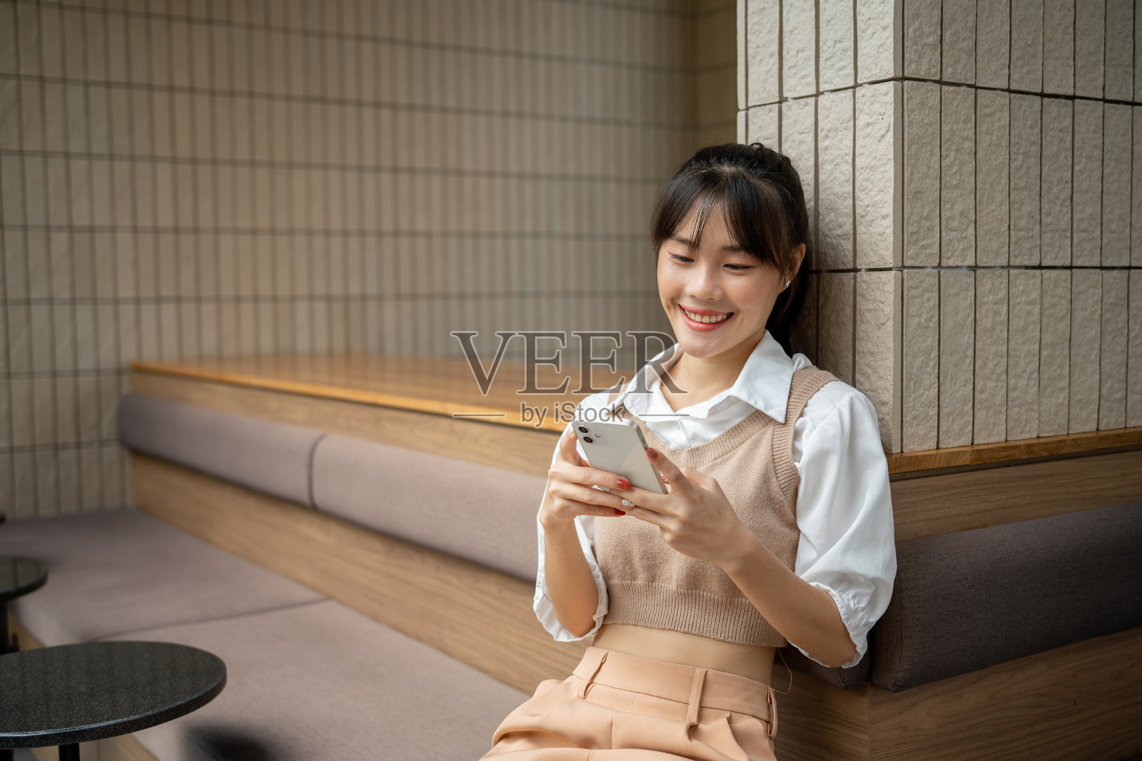 一位快乐的亚洲女性在室内放松的同时，正在用智能手机和朋友聊天。照片摄影图片