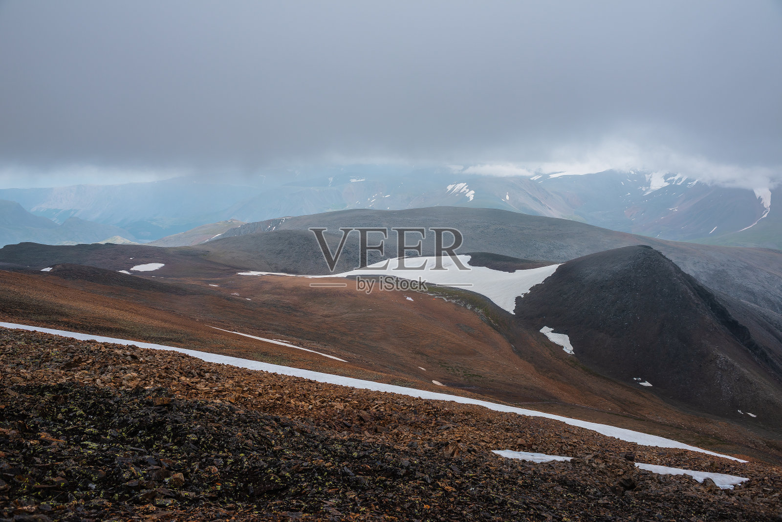 阴暗多云的景观与高山口，宽阔的冰川在石质山坡和雪山的轮廓在阴雨低云远。在恶劣的天气里，灰色的天空下有大雪的大山。照片摄影图片