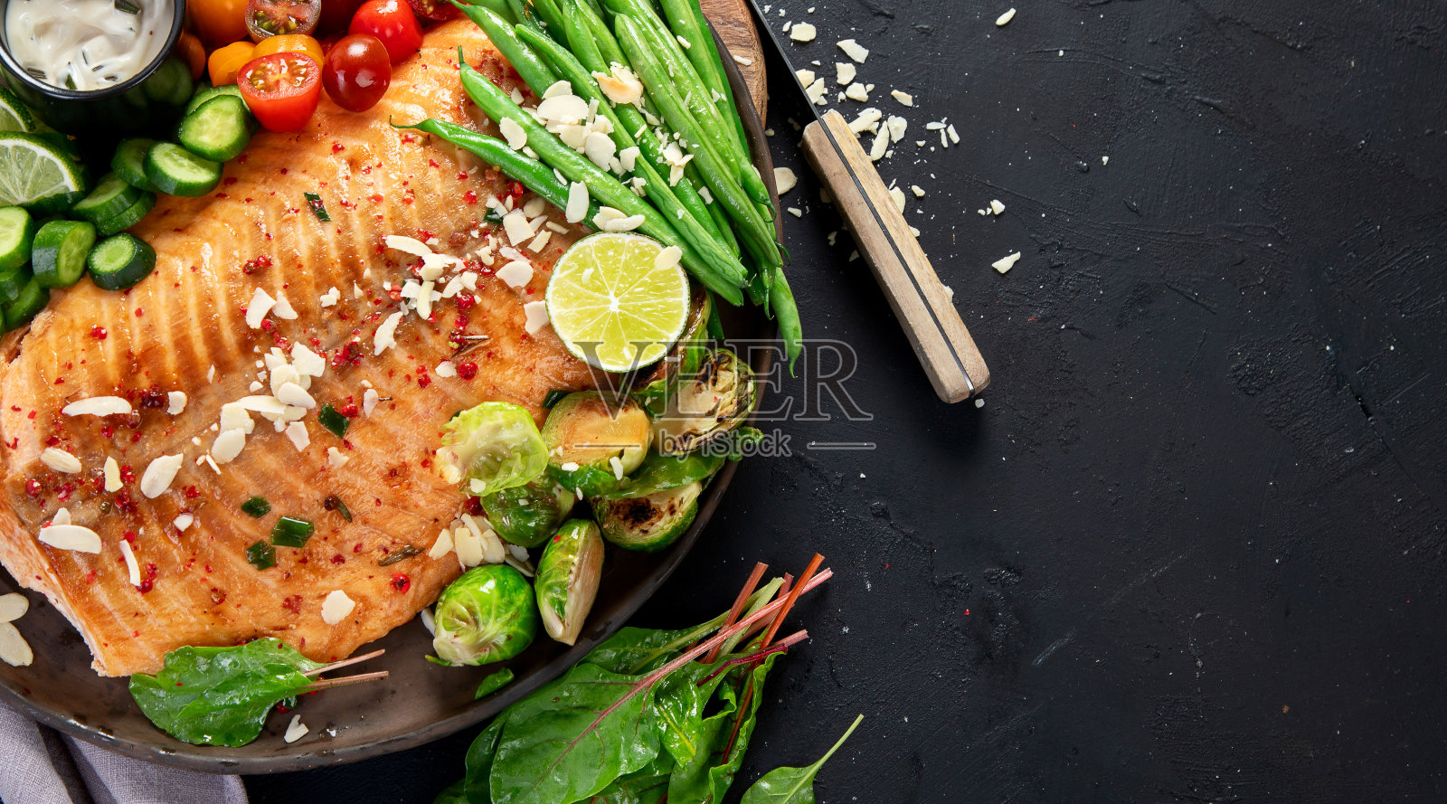 煮鲑鱼配新鲜蔬菜，酸橙和鱼源。烤鱼在黑暗的背景照片摄影图片