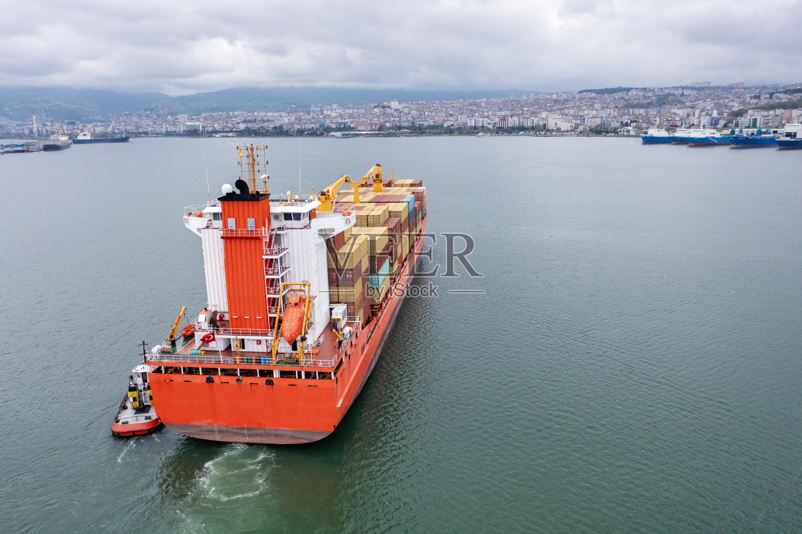载运集装箱的货轮鸟瞰图，货轮正与拖船一起将进口货物运至货箱码头供海关查验。物流运输和航运的概念。照片摄影图片