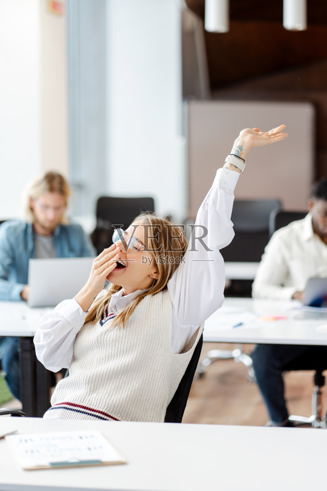 年轻的女商人在办公桌前打着哈欠，伸着懒腰，工作累了照片摄影图片