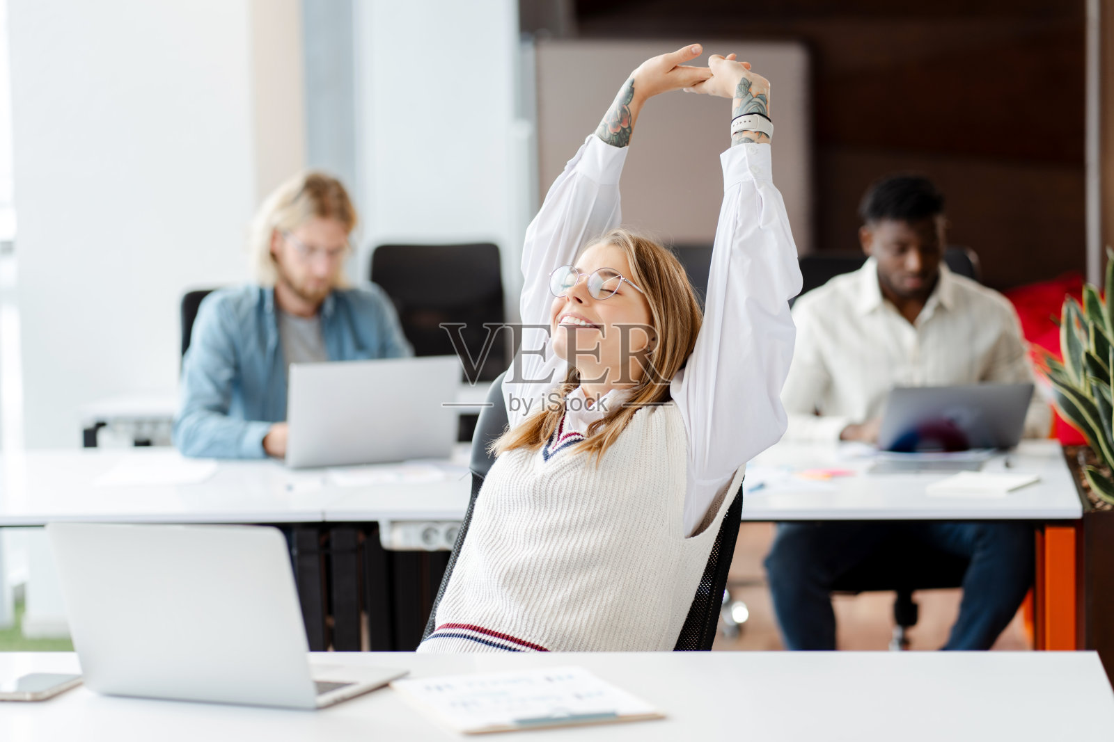 快乐的女商人在工作场所伸懒腰，桌上放着笔记本电脑照片摄影图片
