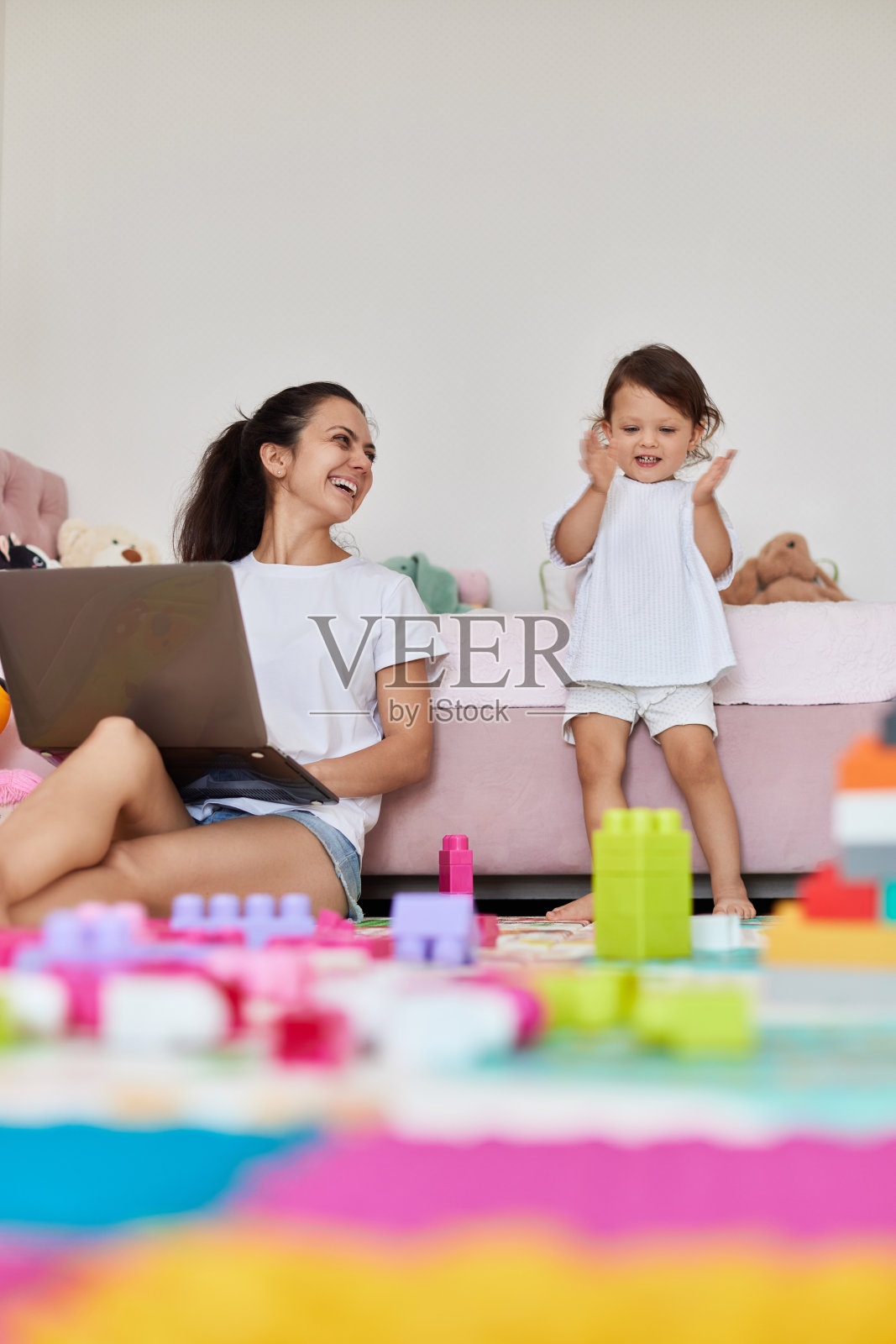 女婴在玩积木玩具，母亲坐在地板上摆弄笔记本电脑照片摄影图片
