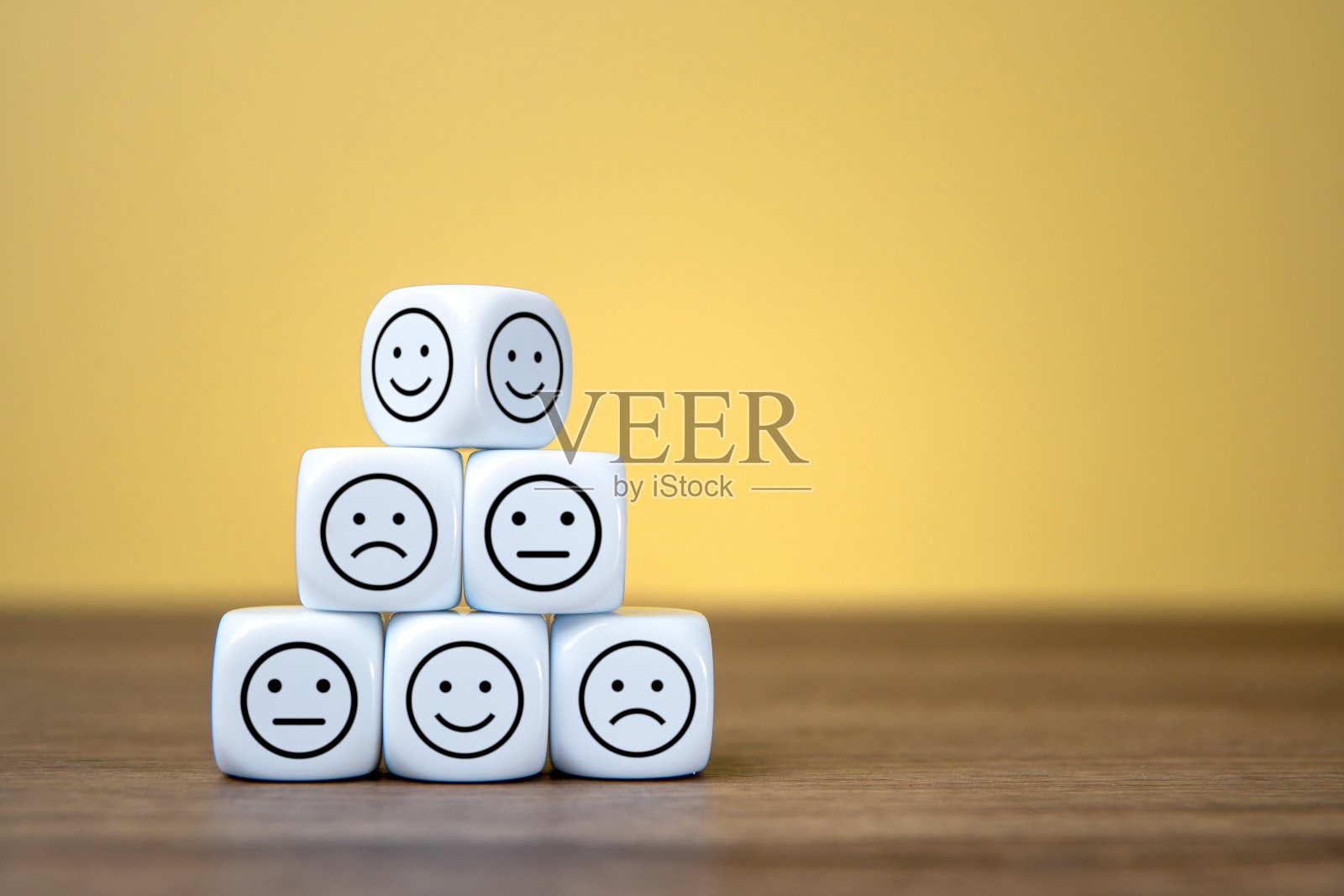 有快乐、中性和悲伤表情的白色骰子堆叠在一个木制的表面上。照片摄影图片