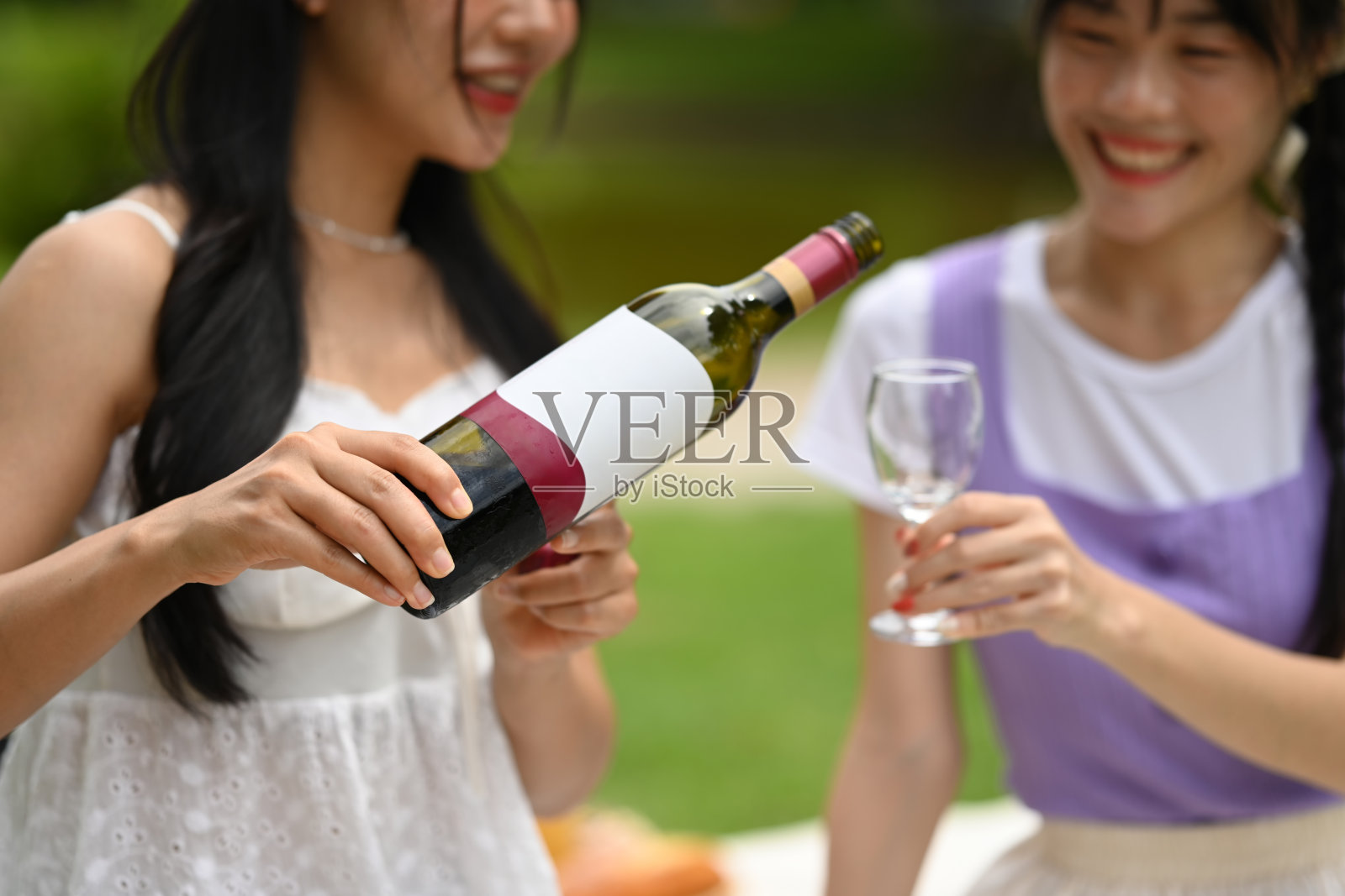 年轻的亚洲女子在和朋友在公园野餐时把酒倒进杯子里照片摄影图片