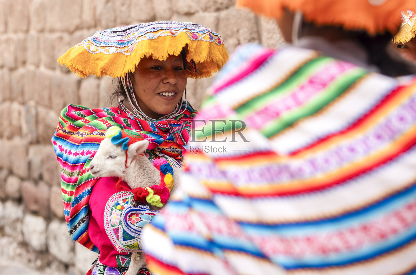 库斯科的土著妇女，穿着漂亮的彩色衣服，展示小羊羔，并收取几枚硬币拍照。照片摄影图片