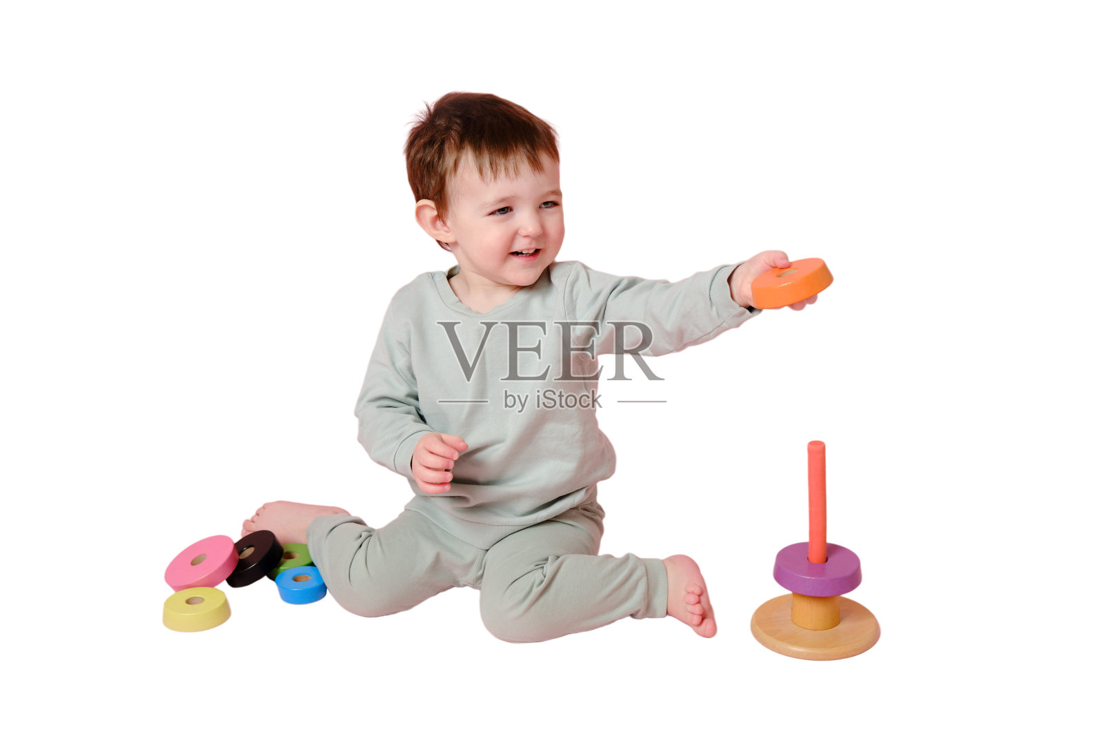 快乐的蹒跚学步的婴儿在工作室里玩金字塔，孤立在白色的背景上。小男孩把木环放在玩具金字塔上。孩子一岁八个月，身高正常照片摄影图片