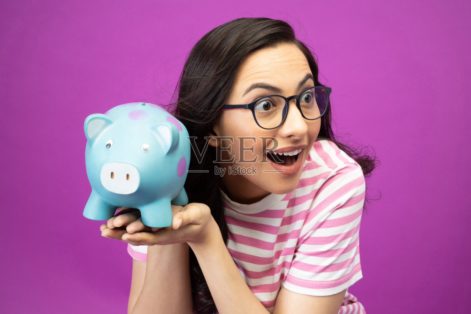 照片漂亮的年轻女子银行猪显示是t恤孤立的紫色背景股票照片照片摄影图片