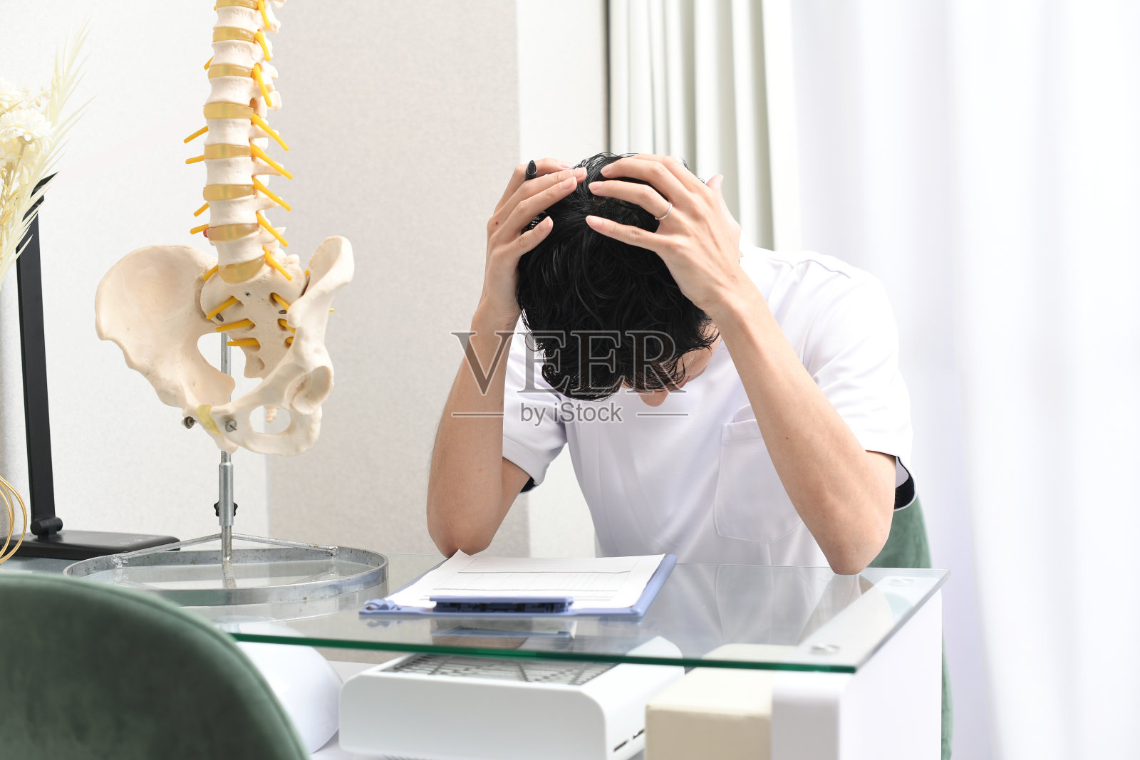 一位身穿白大褂的亚洲男性按摩师抱着头，忧心忡忡照片摄影图片