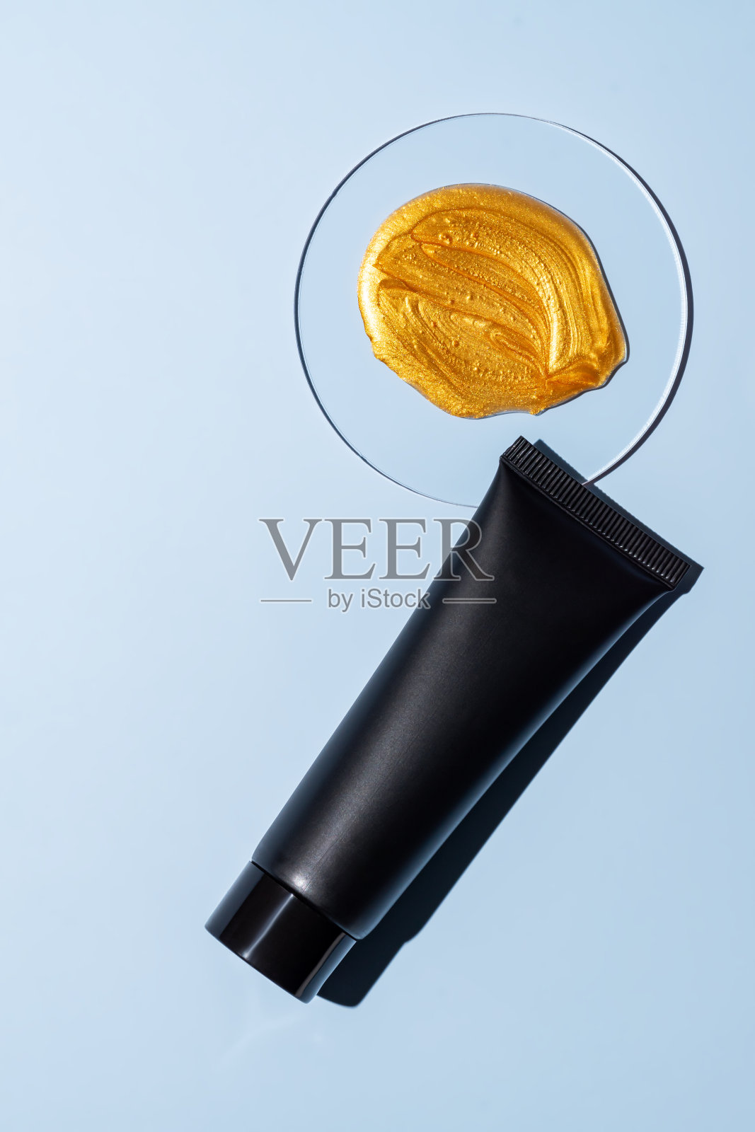 黑色挤压瓶塑料管的模型，用于药品或化妆品的品牌。化妆品瓶容器在蓝色背景旁边的培养皿与黄金面膜涂抹。极简主义照片摄影图片