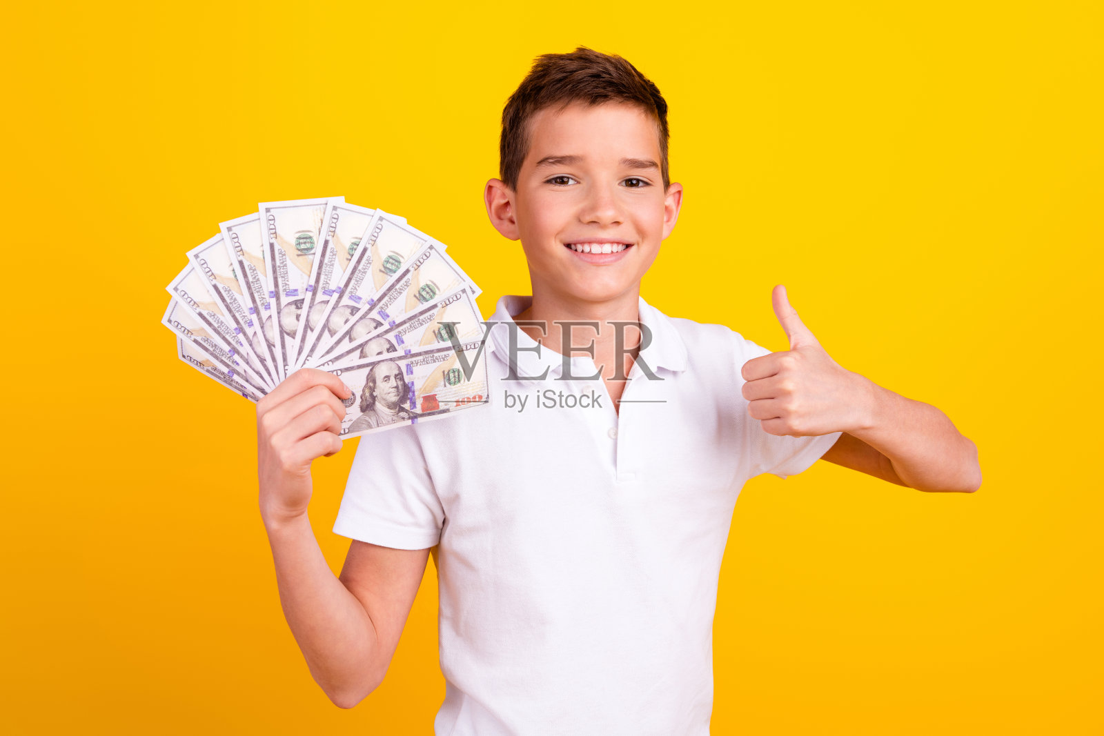 时髦的酷男生穿着polo t恤，拿着现金风扇，拇指朝上，背景是孤立的黄色照片摄影图片