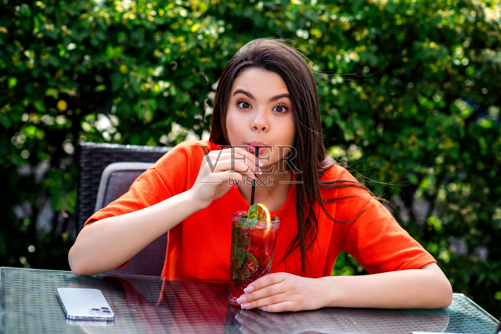 照片积极的青少年可爱的开朗的女人坐在桌子咖啡馆喝鸡尾酒穿红色的衣服散步公园阳光明媚的春天天气外面照片摄影图片