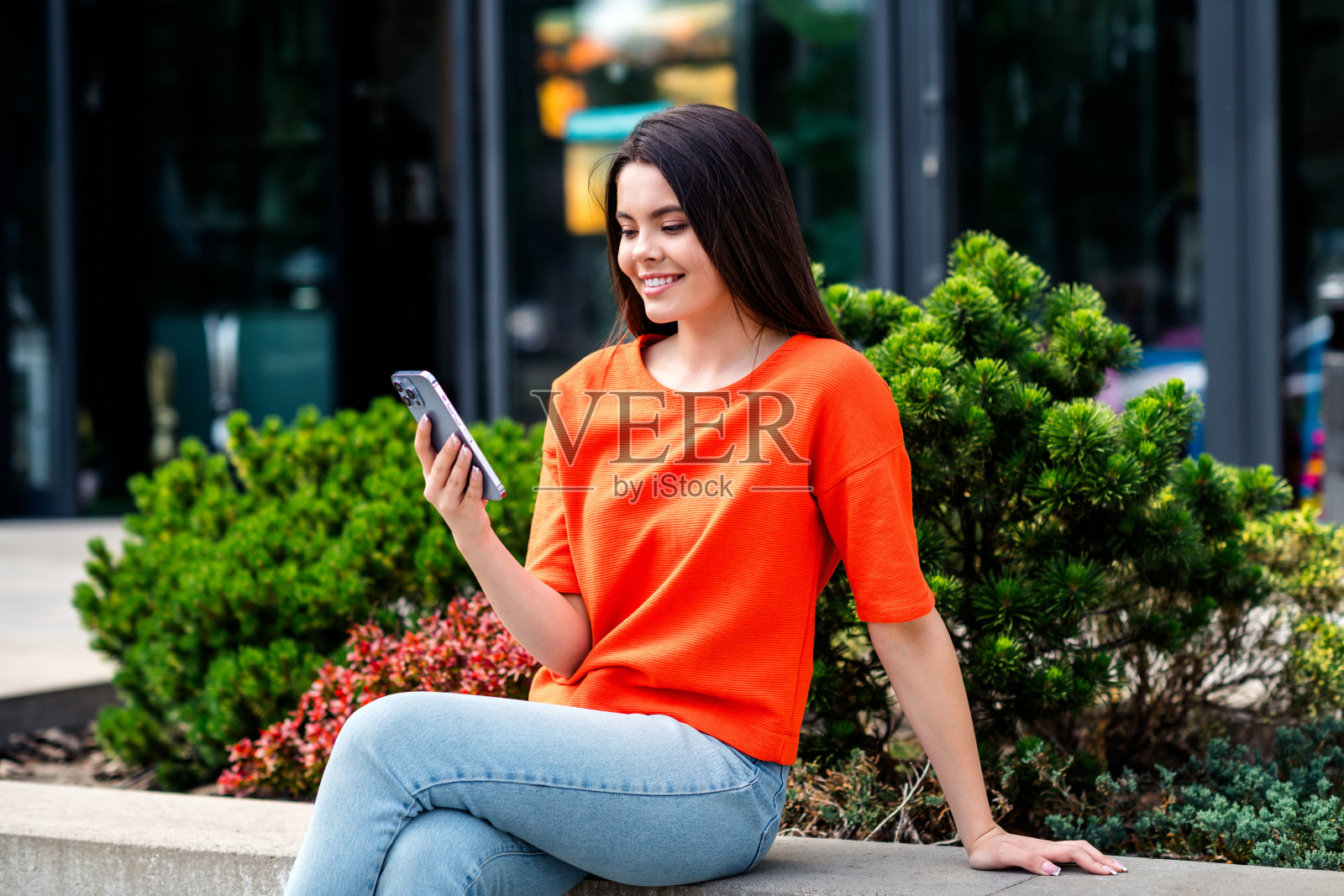 漂亮的青少年照片好心情的女孩坐在户外拿着设备穿着红色的衣服走在城市公园外照片摄影图片