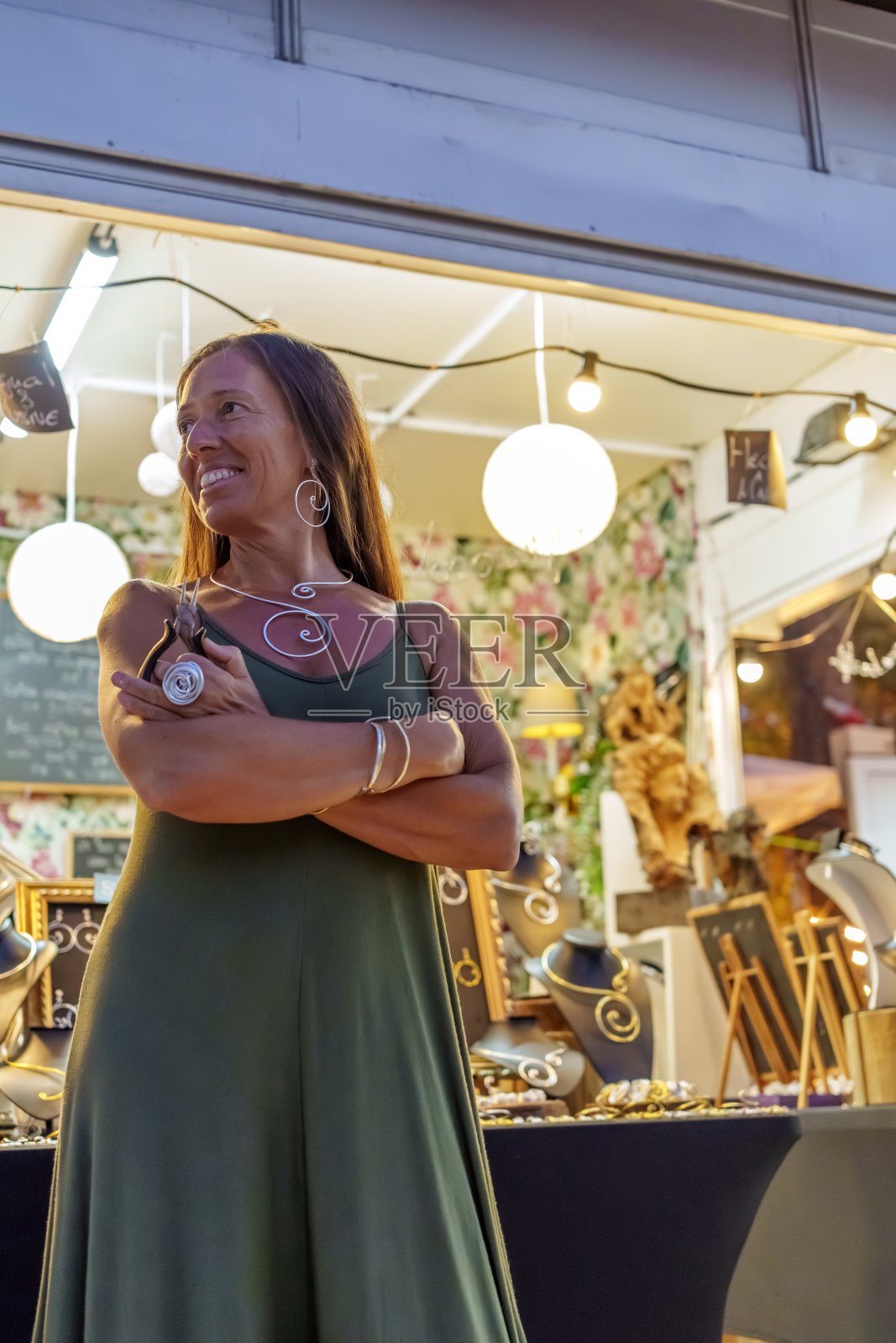 一名妇女在她的街头摊位前摆姿势，手里拿着工具，出售手工铝线珠宝照片摄影图片